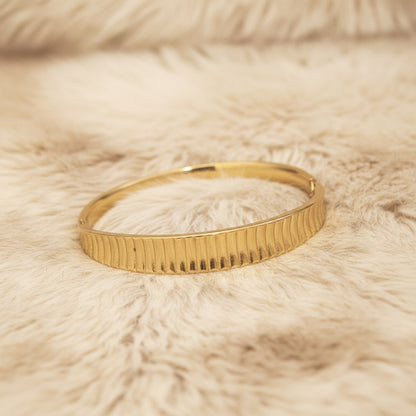 Gold bangle on a textured beige surface