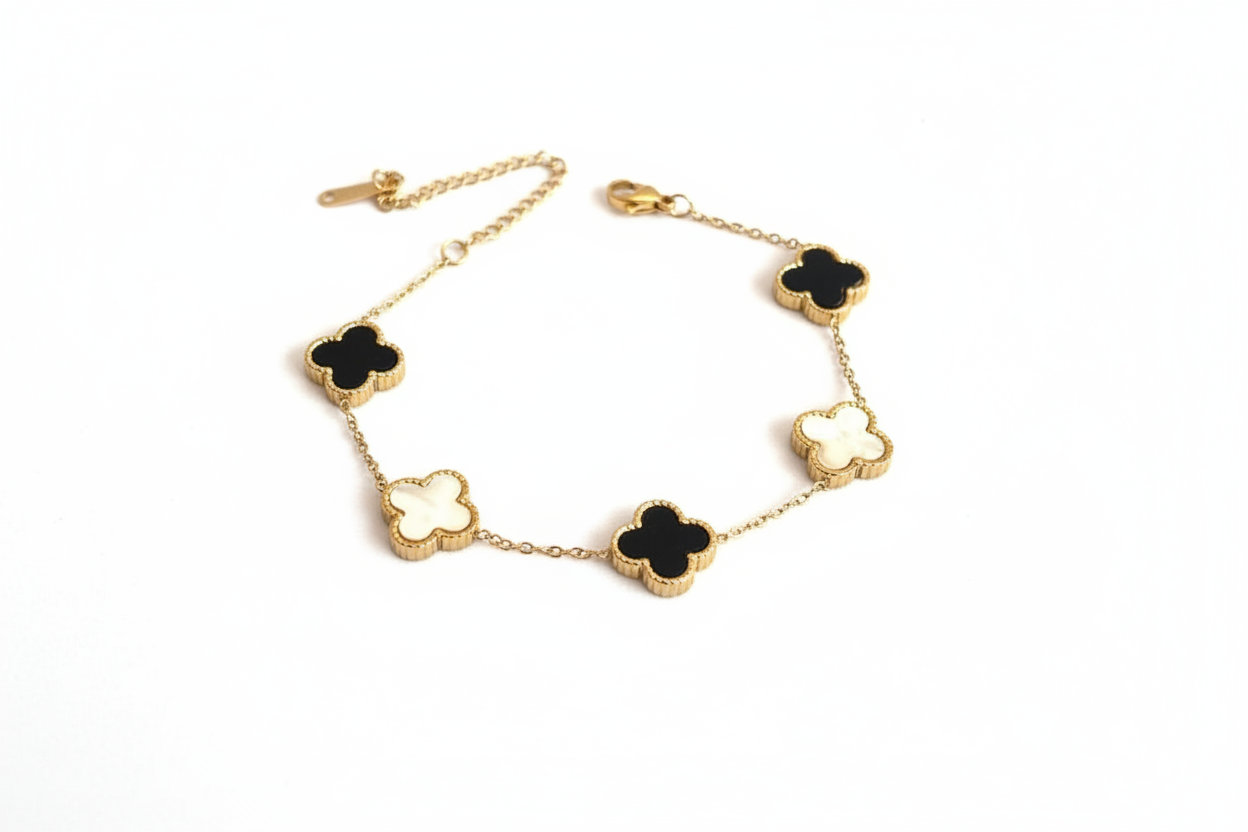 Gold bracelet with black and white clover-shaped charms on a light gray background