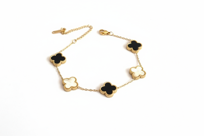 Gold bracelet with black and white clover-shaped charms on a light gray background