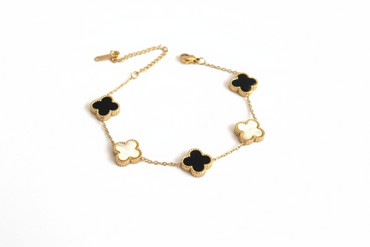 Gold bracelet with black and white clover-shaped charms on a light gray background