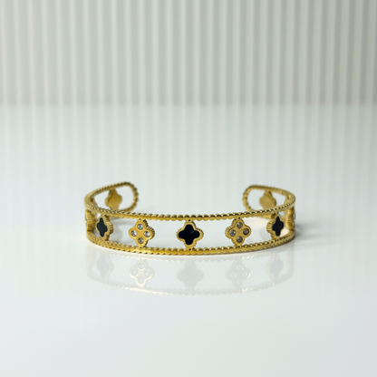 Gold bracelet with black clover designs on a white background